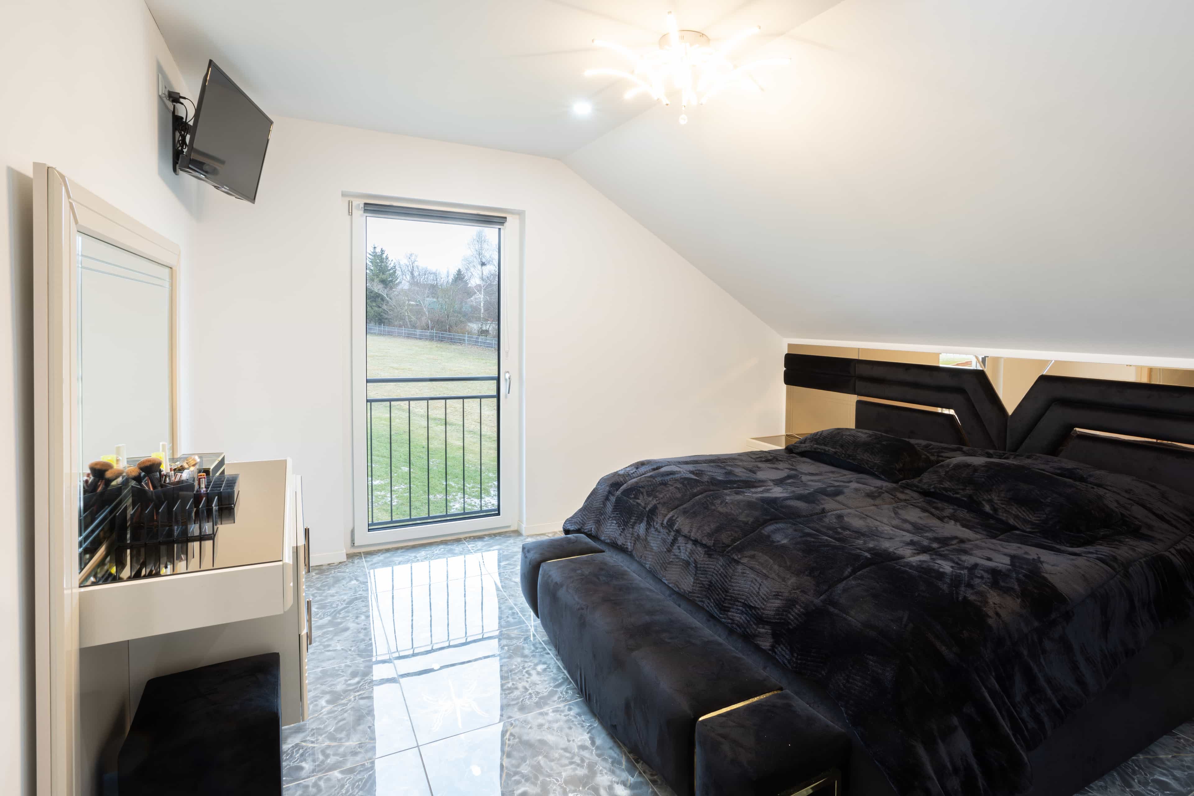 Schlafzimmer mit schwarzem Bett, Marmorboden und Balkontür im Haas Fertighaus der Familie Khalil