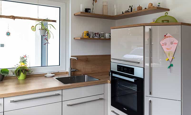 Weiße Küche mit Holzarbeitsplatte, Fenster und Einbaugeräten im Doppelhaus Haas D 112 D