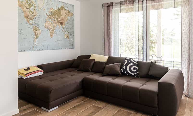 Wohnzimmer mit brauner Eckcouch und Weltkarte an der Wand im Doppelhaus Haas D 112 D