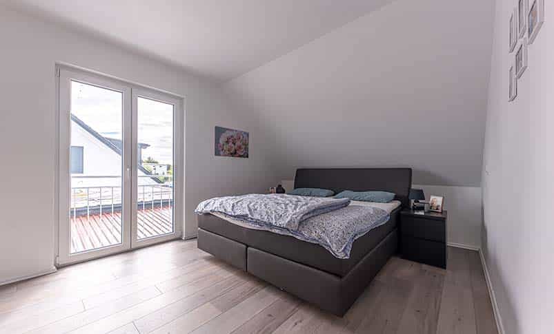 Schlafzimmer unter der Dachschräge mit Boxspringbett und Balkontür im Doppelhaus Haas D 137 B