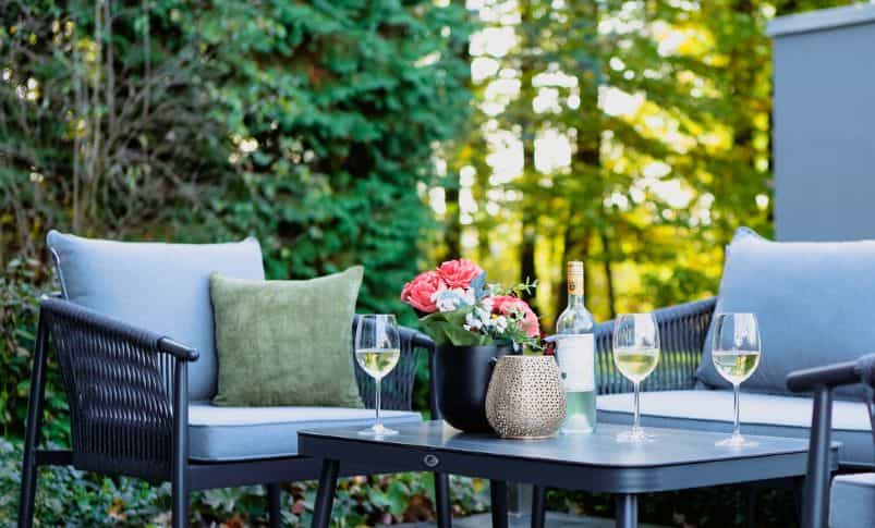 Terrasse mit Loungemöbeln, Weingläsern und Blumen im Grünen, Musterhaus Bad Vilbel nach dem Re-Opening
