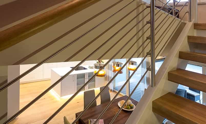 Treppe mit Edelstahlgeländer und Blick in die Küche im Fertighaus Haas TL 156 im Bauhausstil