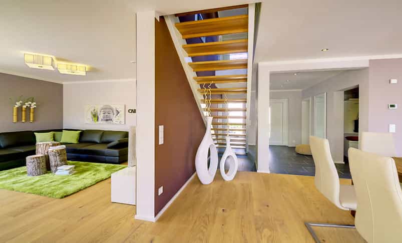 Wohnzimmer mit offener Treppe, schwarzer Couch und grünem Teppich im Kubushaus Haas TL 156