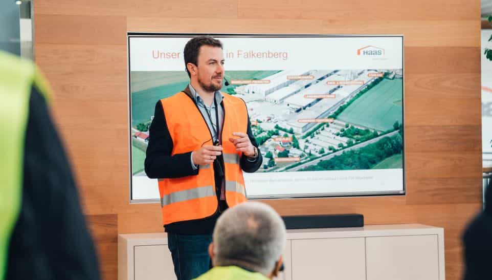 Vortrag in Warnweste vor dem Luftbild des Haas Fertigbau Werks in Falkenberg bei der IHK-Gremiumssitzung