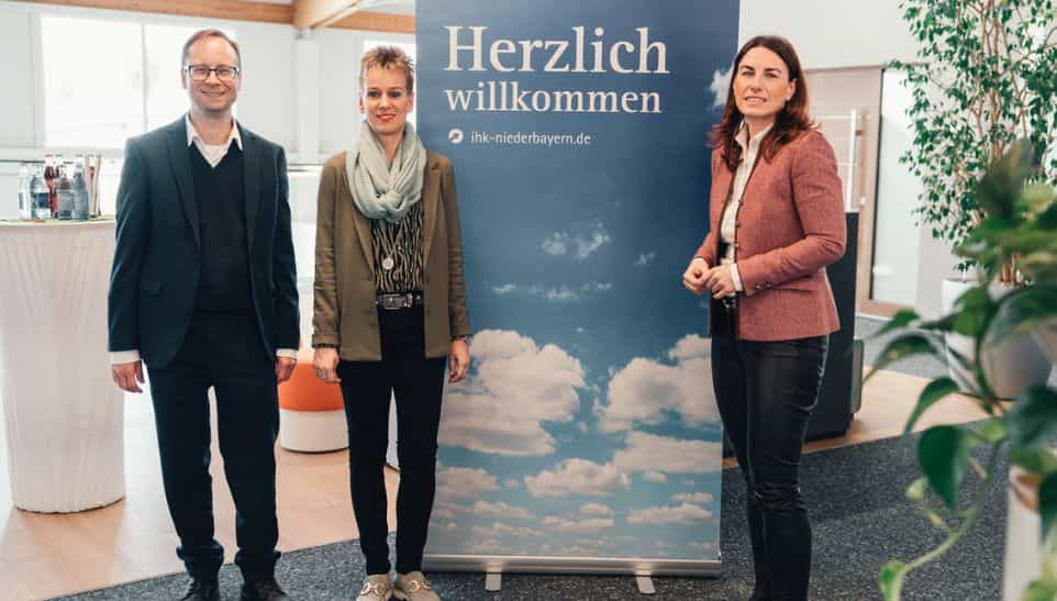 Drei Personen vor dem Herzlich-willkommen-Banner der IHK Niederbayern bei Haas Fertigbau in Falkenberg