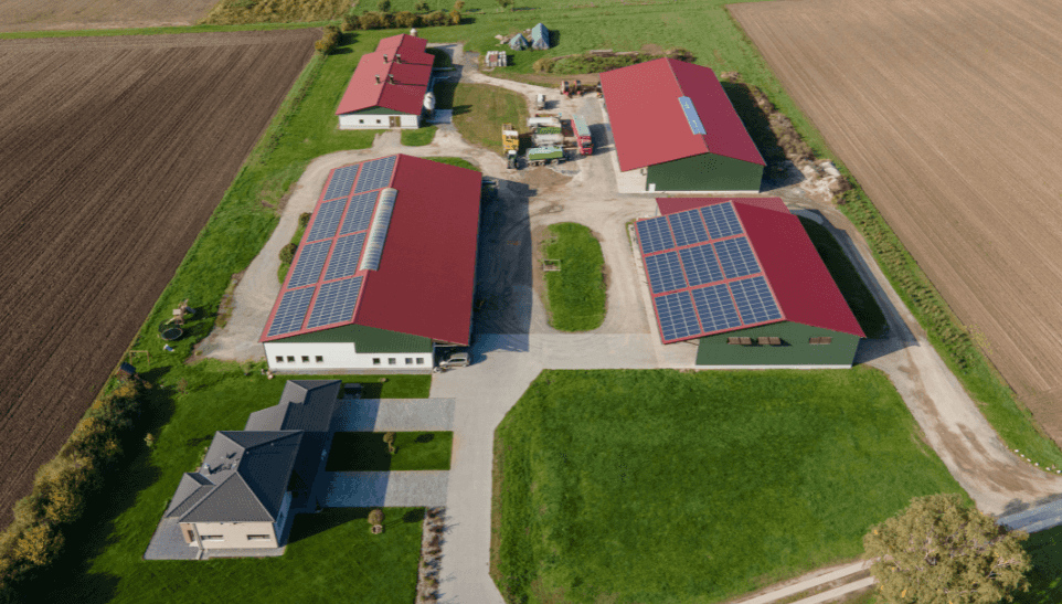 Luftaufnahme eines Hofes mit roten Hallendächern und Photovoltaikmodulen, PV-Systemhalle von Haas auf der Rottalschau