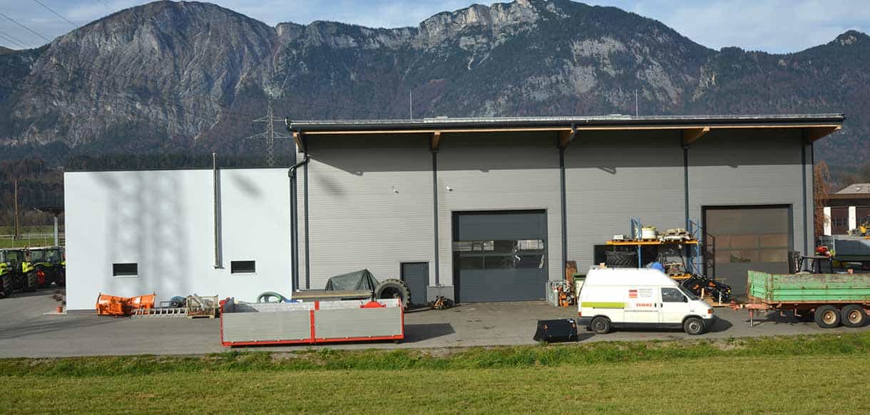 Hallenrückseite von Landtechnik Embacher mit Landmaschinen vor Tiroler Bergen