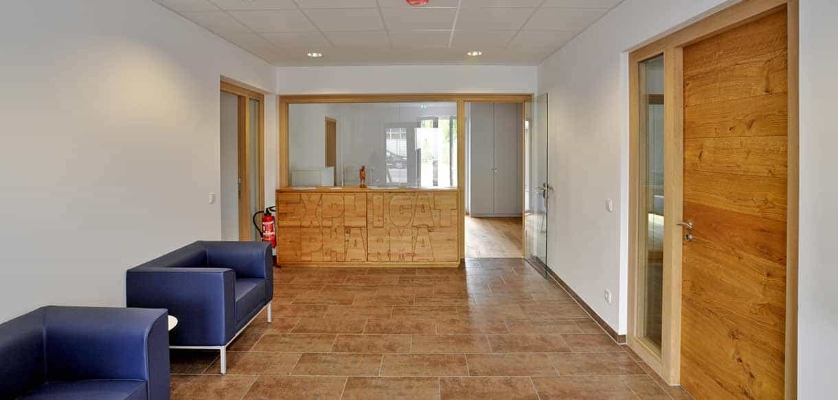 Empfangsbereich mit blauem Sofa, Holztresen und Parkett im Bürogebäude von Explicat Pharma