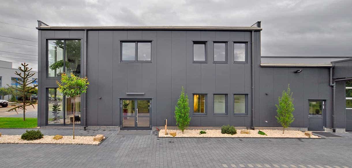 Frontansicht des Bürogebäudes mit Lagerhalle von RM Bodenbeläge mit gepflastertem Parkplatz