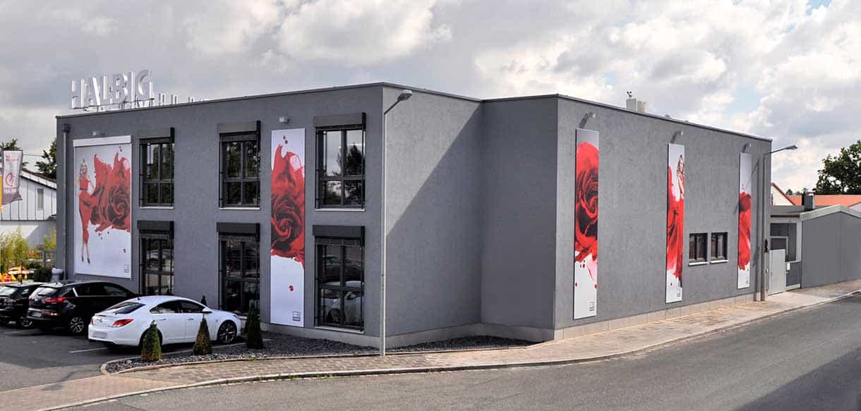 Seitenansicht des Verkaufsgebäudes von 1A Blumen Halbig mit grauer Fassade und Rosenbannern