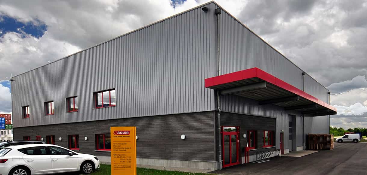 Seitenansicht der Lagerhalle von Adler Lacke mit Büro- und Sozialbereich, rotem Vordach und Parkplatz
