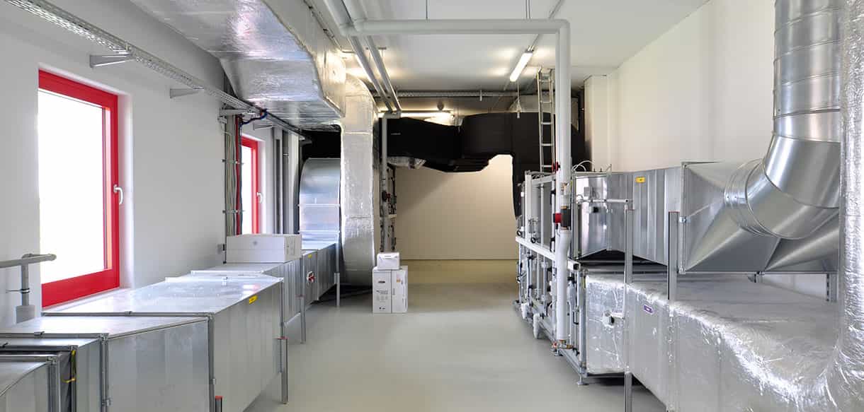 Technikbereich mit verzinkten Lüftungskanälen und roten Fenstern im Gebäude von Adler Lacke