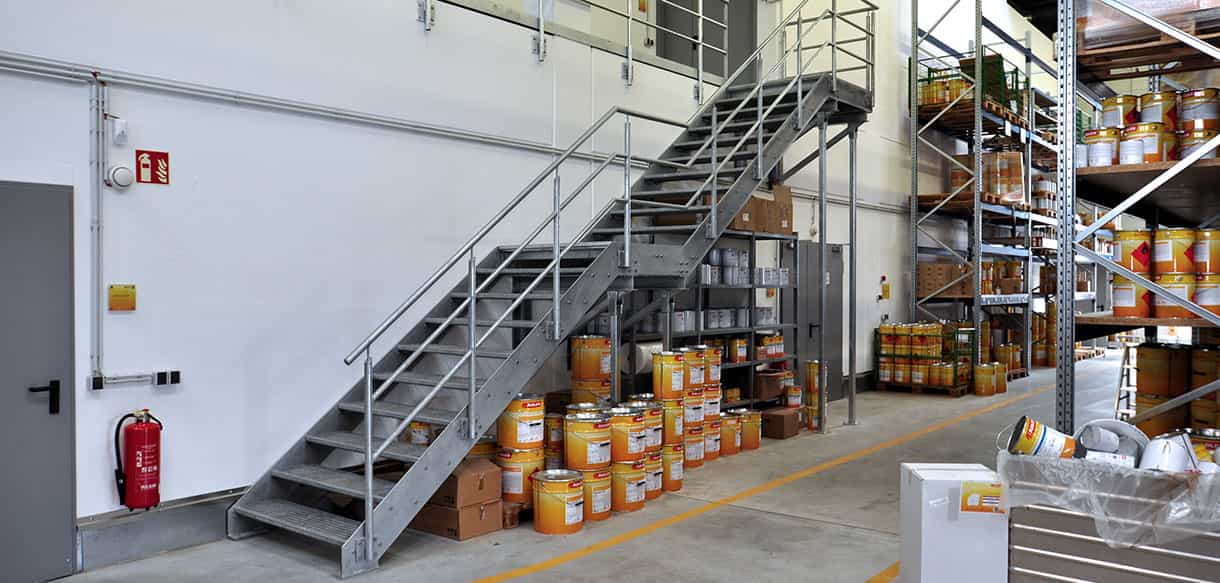 Stahltreppe zur Lagerebene mit Lackeimern und Regalen im Lacklager von Adler Lacke