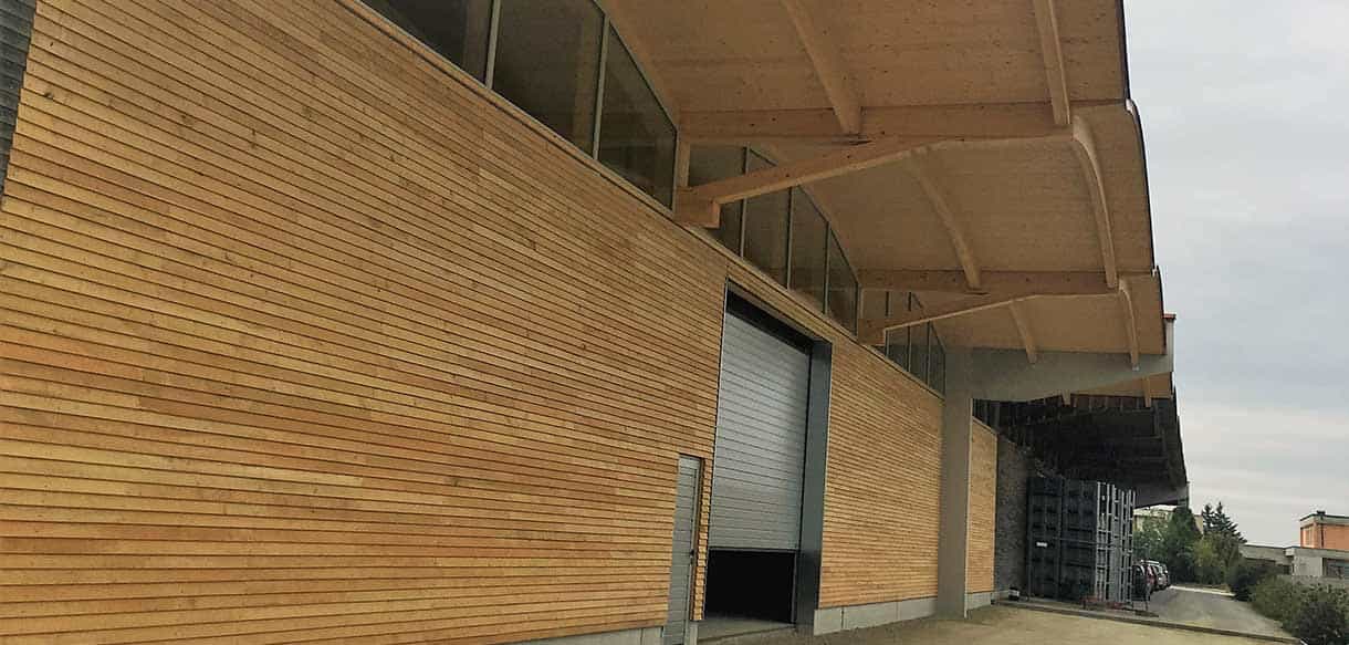 Holzfassade mit Rolltor und geschwungenem Dachüberstand an der Lagerhalle von Scheibelhofer Reben