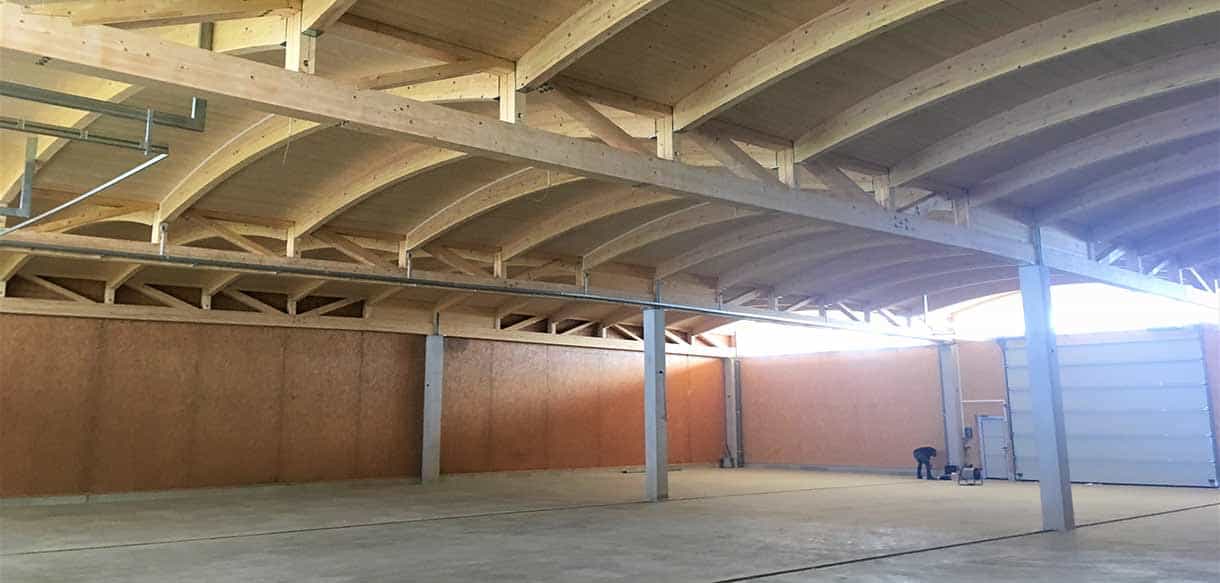 Halleninneres mit bogenförmigen Leimholzbindern und Holzwänden der Lagerhalle Scheibelhofer Reben