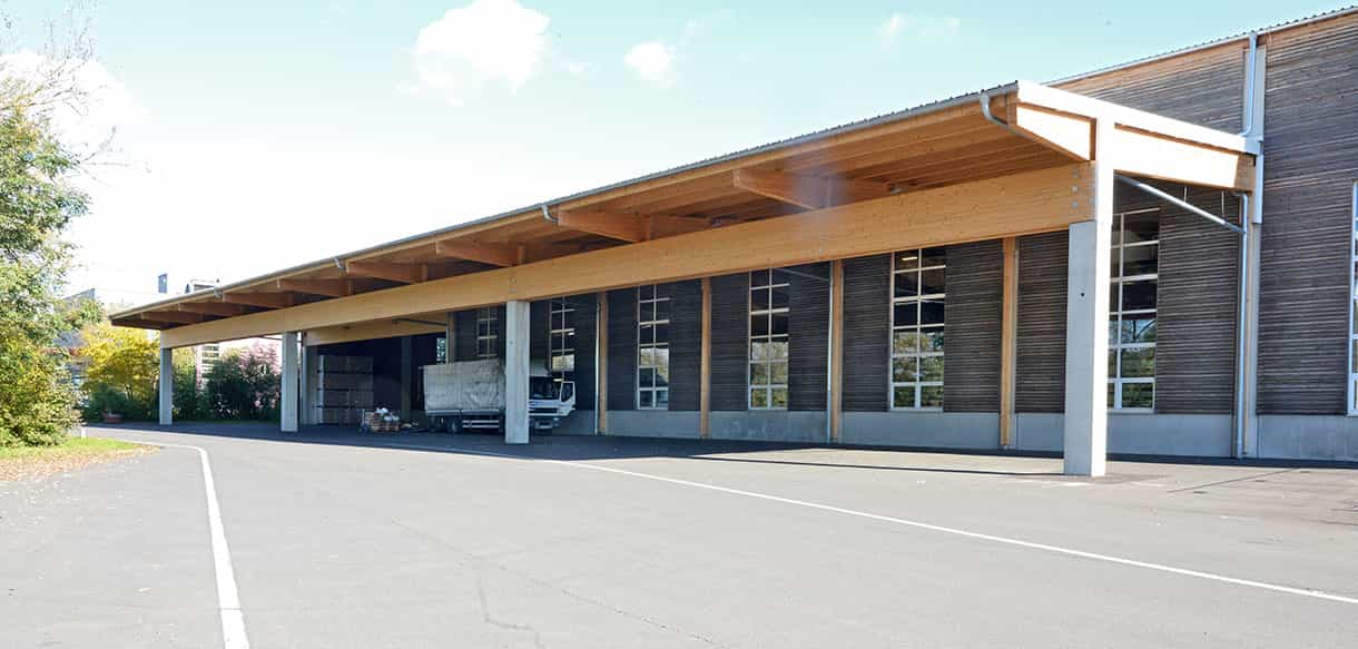 Weit auskragendes Vordach aus Holz an der Lagerhalle Scheucher mit überdachtem Ladebereich und Lkw