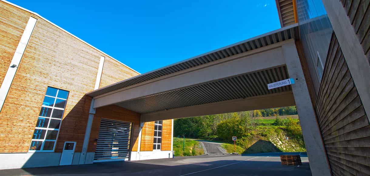 Blick unter das Vordach der Lagerhalle Scheucher Holzindustrie auf Hallentor und Holzfassade