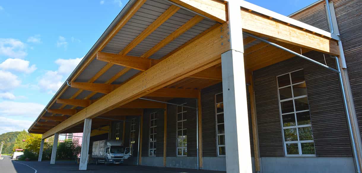 Vordach mit Brettschichtholzträgern an der Lagerhalle Scheucher Holzindustrie, darunter ein Lkw beim Beladen