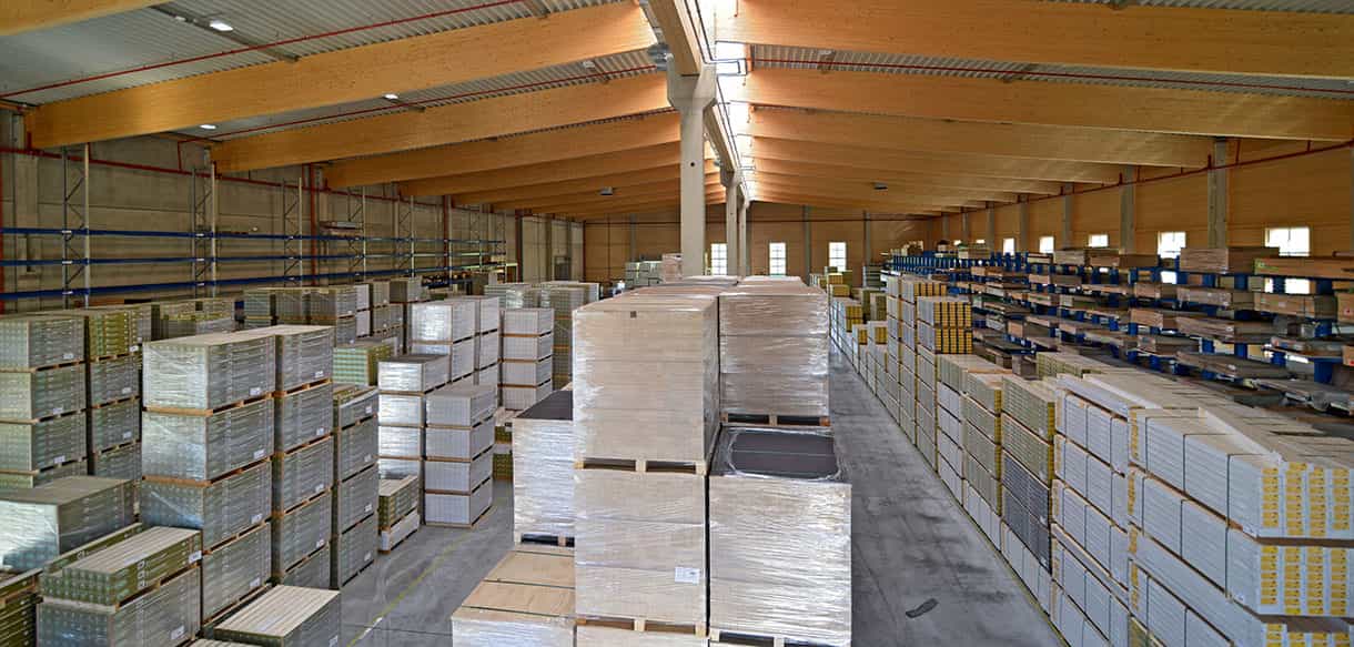 Innenansicht der Lagerhalle Scheucher Holzindustrie mit gestapelten Holzplatten und Regalen unter dem Holzdach