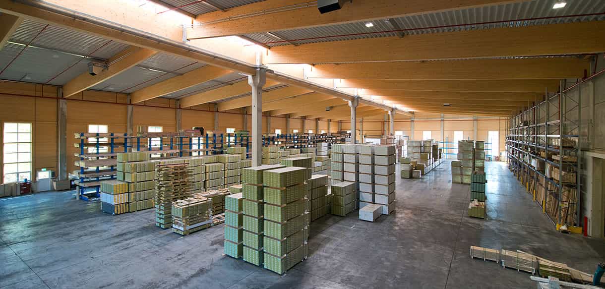 Weitwinkelblick in die Lagerhalle Scheucher Holzindustrie mit gelagerten Holzstapeln unter der Holzdecke