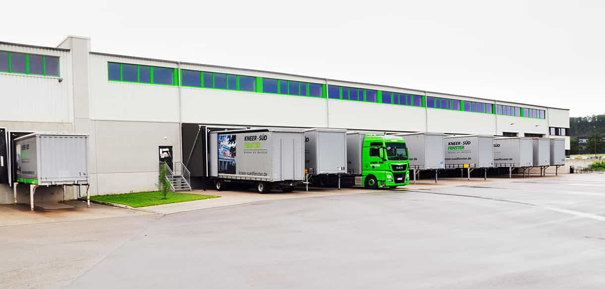 Längsseite der Versandhalle Süd-Fensterwerk mit grünem Fensterband und Lkw an den Verladestationen
