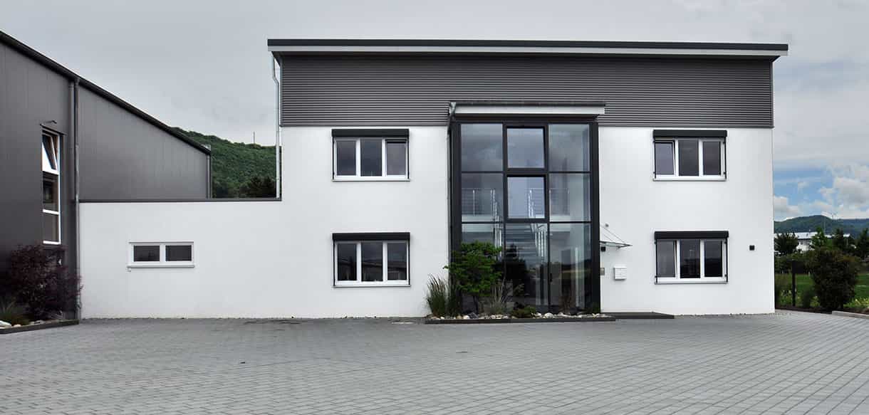 Frontansicht des Bürogebäudes von APA-Tec mit verglastem Eingangsbereich und weißer Fassade