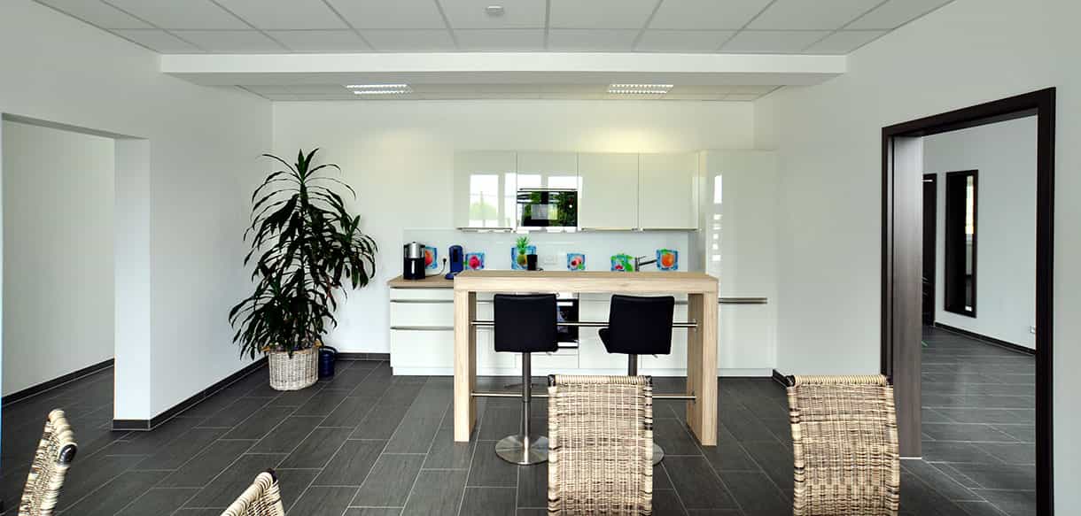 Küchenbereich mit weißer Einbauküche und Stehtisch im Sozialraum von APA-Tec, Innenansicht