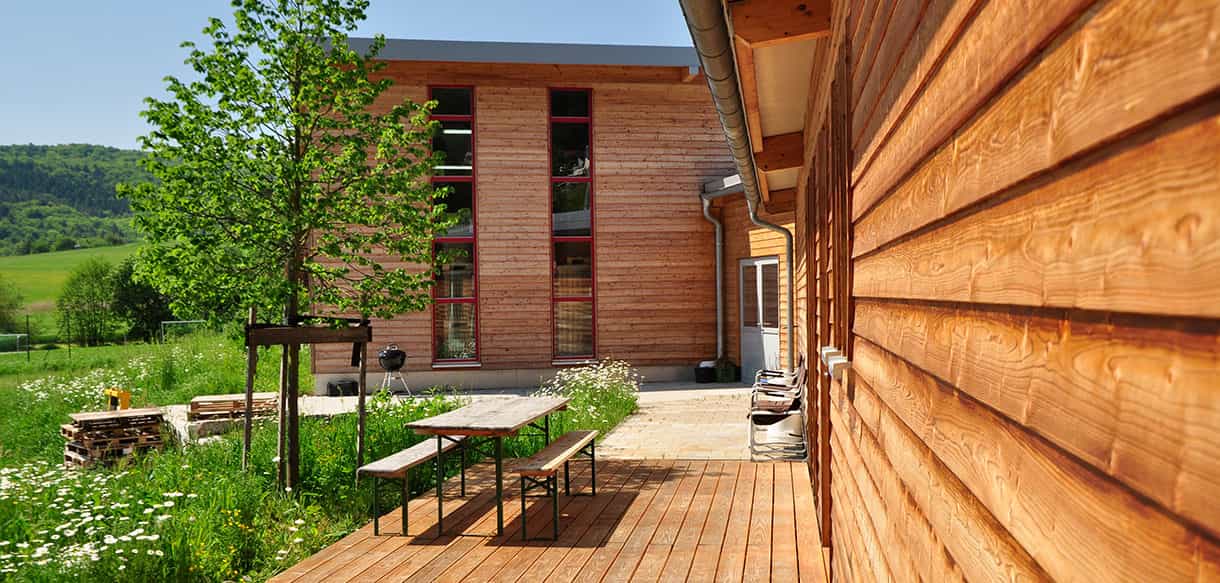 Holzterrasse mit Tisch und Bänken an der Holzfassade der Lagerhalle der Beerenbauern