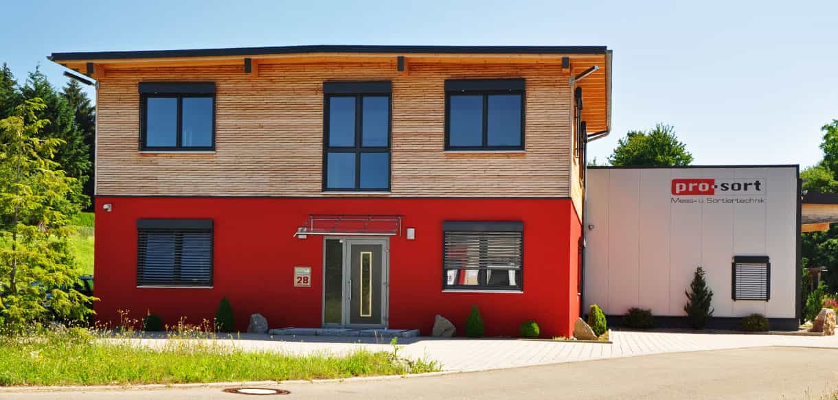Aufgestocktes Bürogebäude mit roter Fassade und Holzverkleidung im Obergeschoss neben der Produktionshalle, Haas Gewerbebau