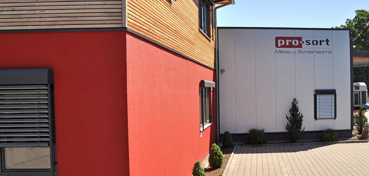 Fassadendetail mit rotem Putz, Holzaufstockung und weißer Hallenwand beim Metallwaren-Hersteller