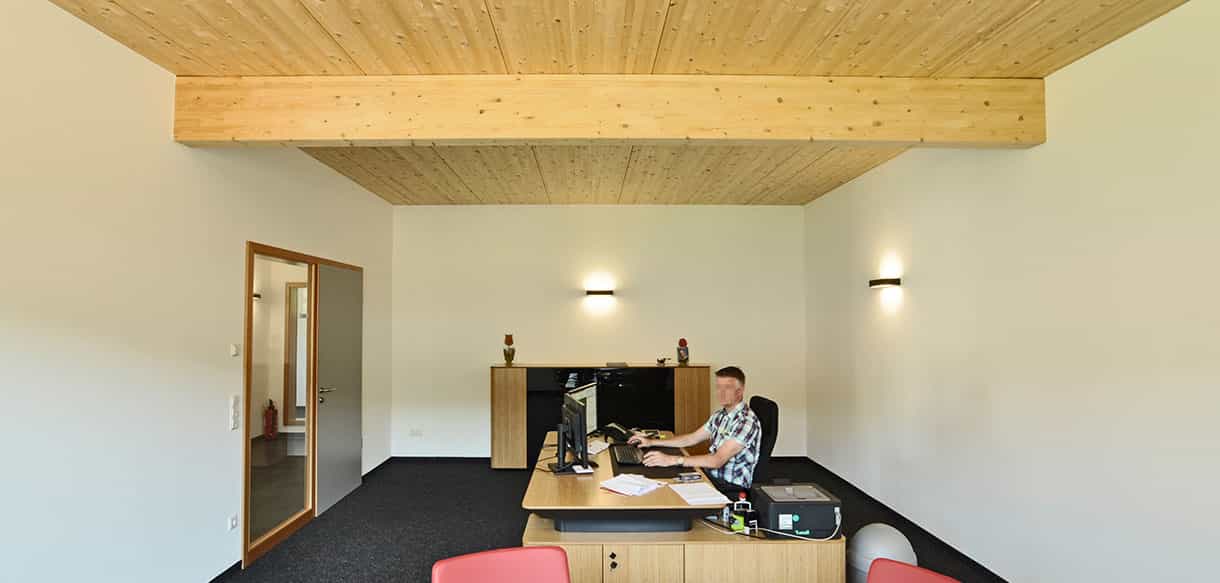 Büro mit Holzdecke und Mitarbeiter am Schreibtisch im aufgestockten Bürogebäude von Haas Gewerbebau