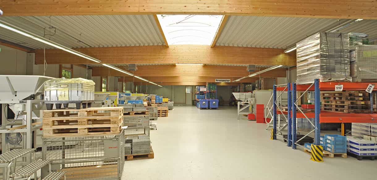 Halleninneres der Produktionshalle mit Leimholzbindern, Lichtband und Palettenregalen