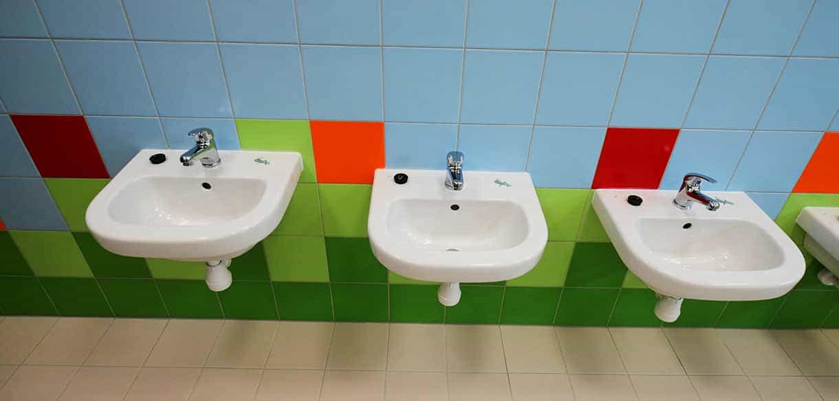 Waschbeckenreihe mit grün-roten Fliesen im Sanitärbereich des Kindergartens Roztoky