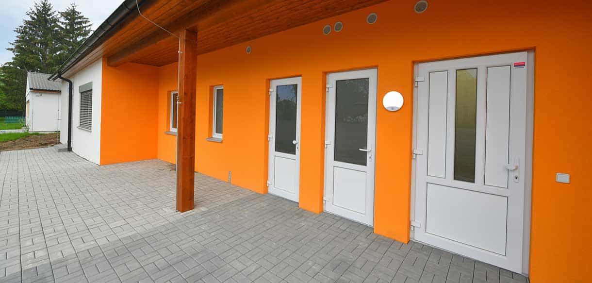 Überdachter Eingang mit oranger Fassade und weißen Türen am Kindergarten Roztoky