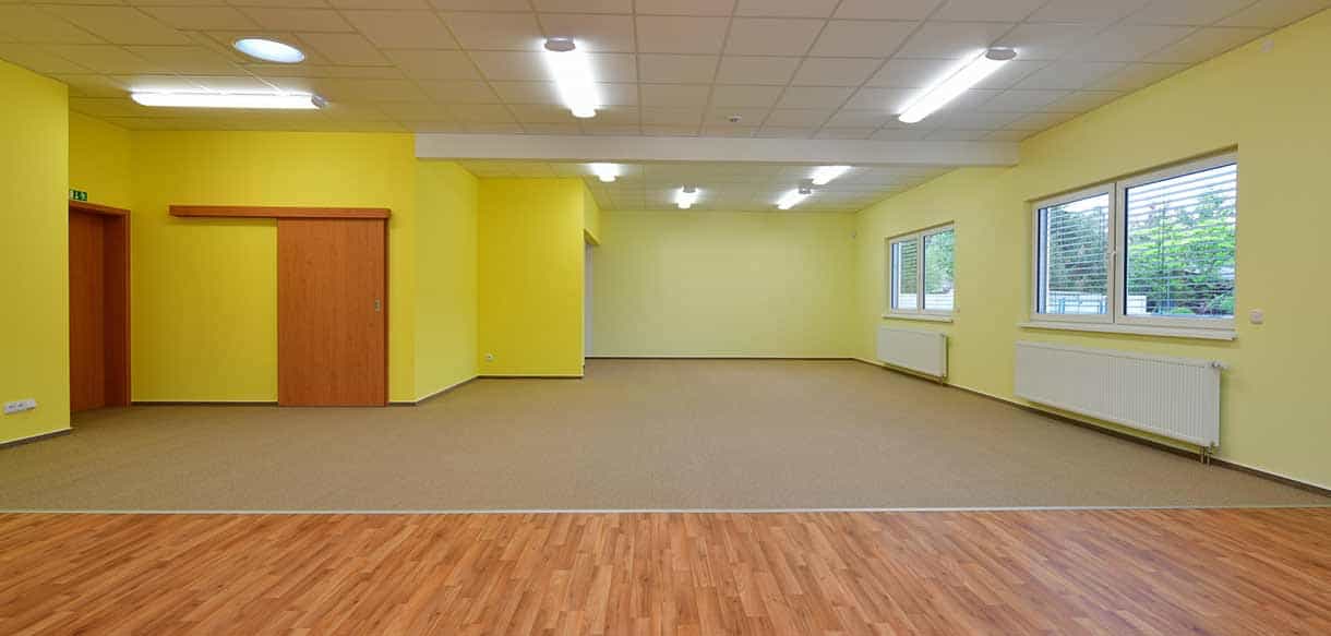 Leerer Gruppenraum in Gelb und Grün mit Holzboden im Kindergarten Roztoky