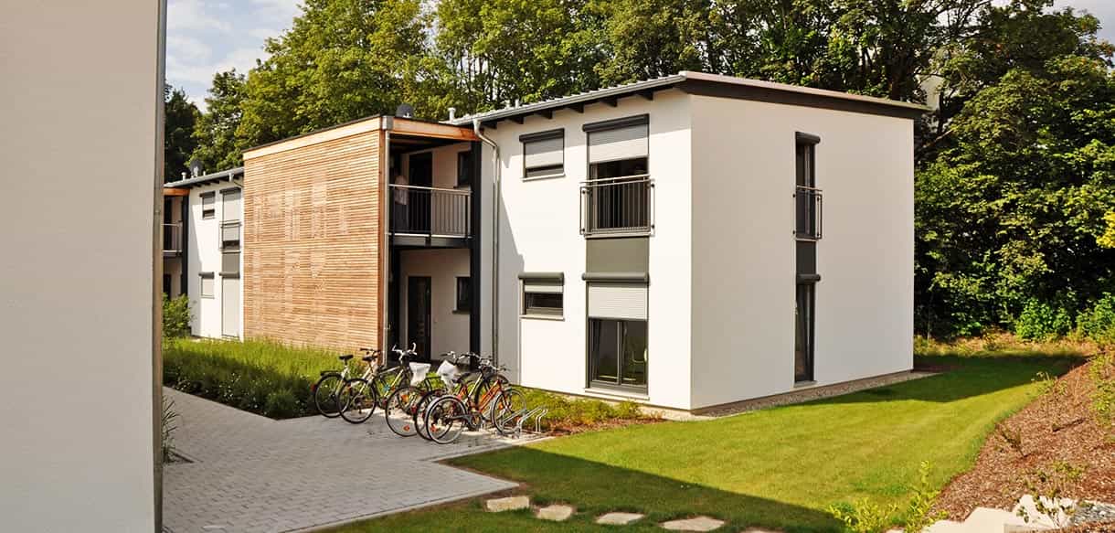 Rückseite des Arbeiterwohnheims Ammer in Taufkirchen/Vils mit weißer Fassade, Balkonen und Fahrradständern