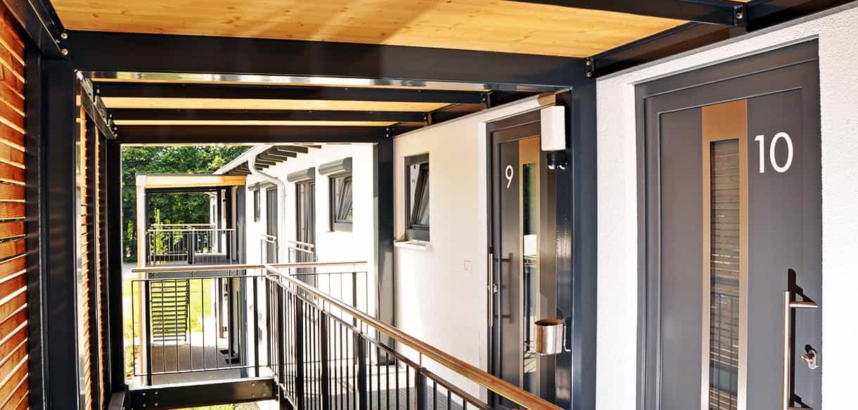 Laubengang mit nummerierten Wohnungstüren und Holzdecke im Arbeiterwohnheim Ammer in Taufkirchen/Vils