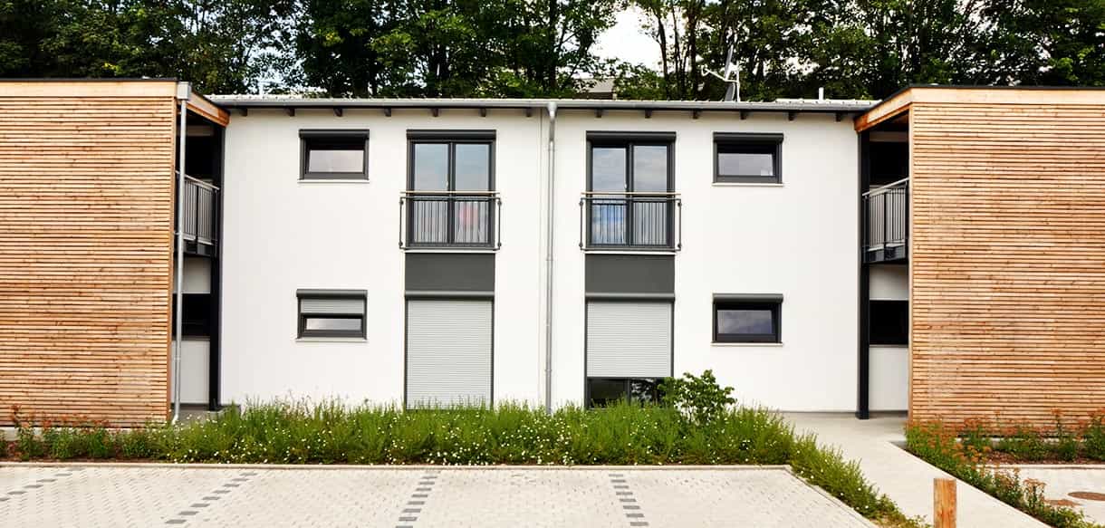 Frontansicht des Arbeiterwohnheims Ammer mit zwei lärchenverkleideten Treppenhäusern und bepflanztem Vorgarten