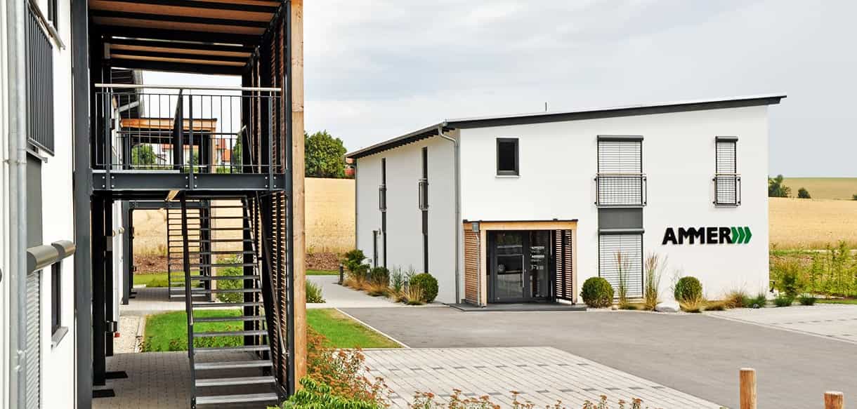 Blick durch das außenliegende Stahltreppenhaus auf das Bürogebäude mit Ammer Logo in Taufkirchen/Vils