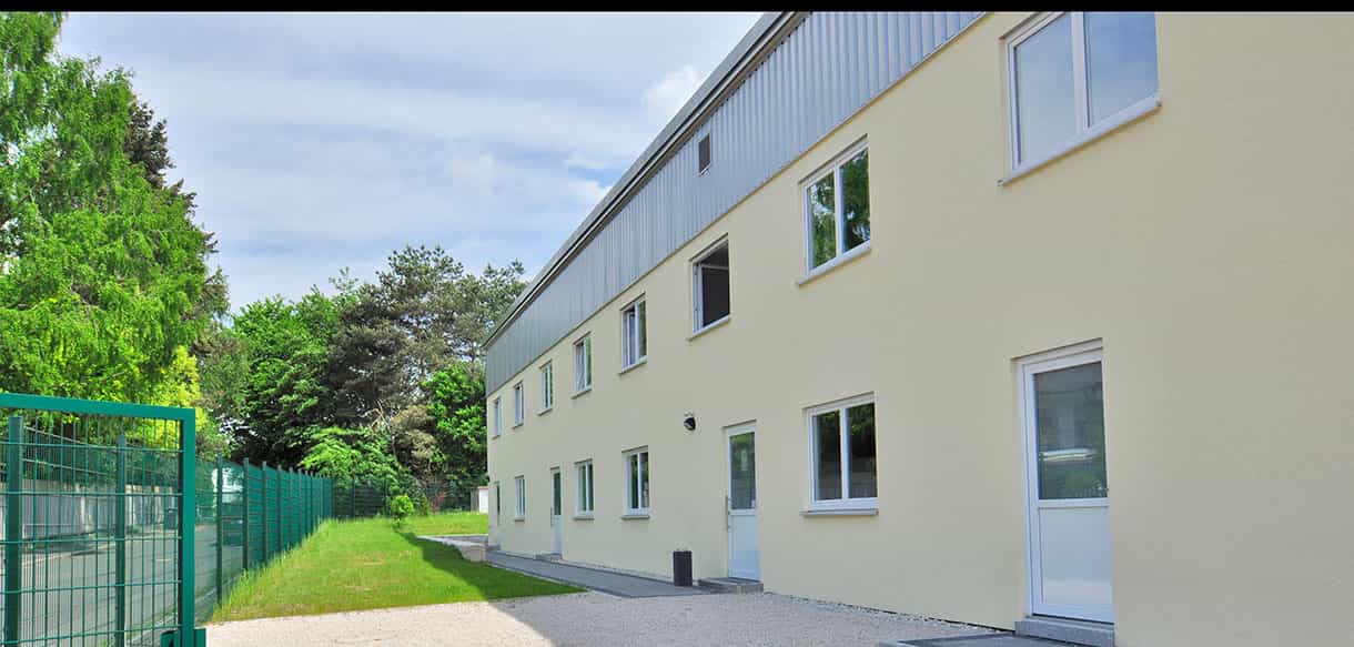 Rückseite des zweigeschossigen Asylbewerberheims mit grünem Zaun und Wiese