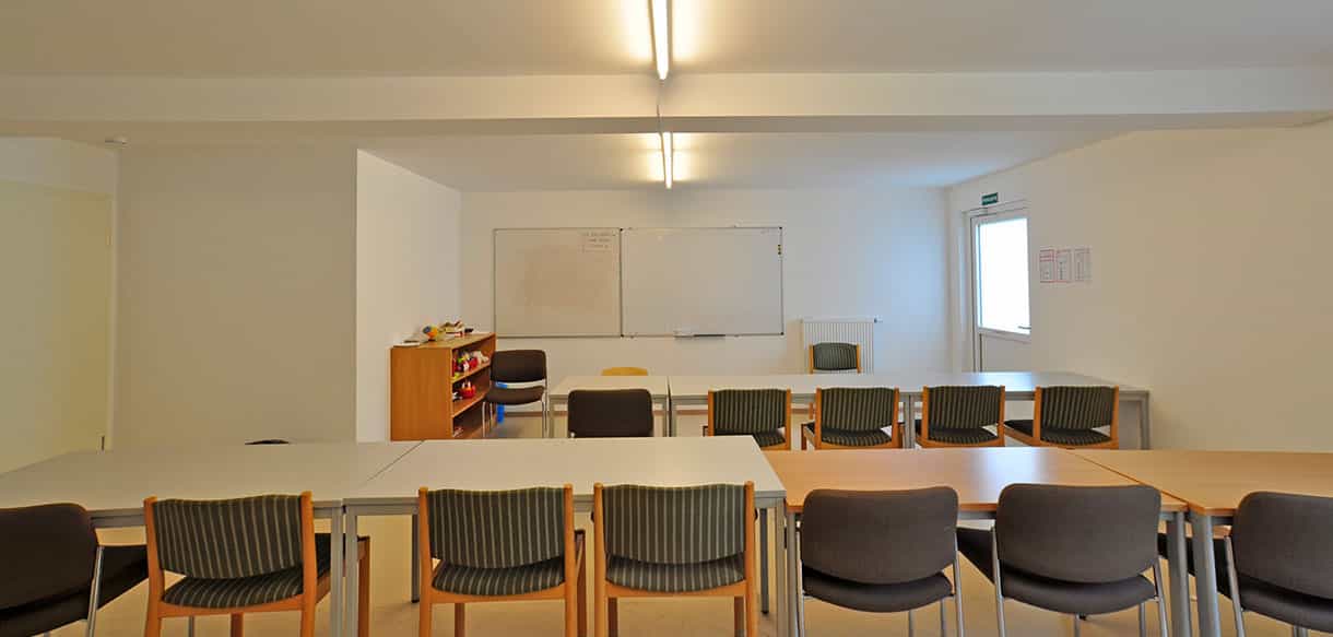 Gemeinschaftsraum im Asylbewerberheim mit langen Tischen, Stühlen und Whiteboard