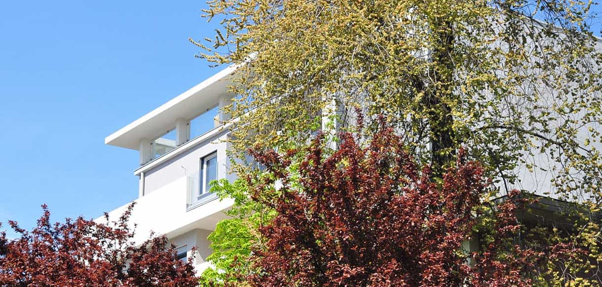 Fassade des Wohngebäudes Alca in Modena mit Balkonen hinter Bäumen, Außenansicht Hausbausatz
