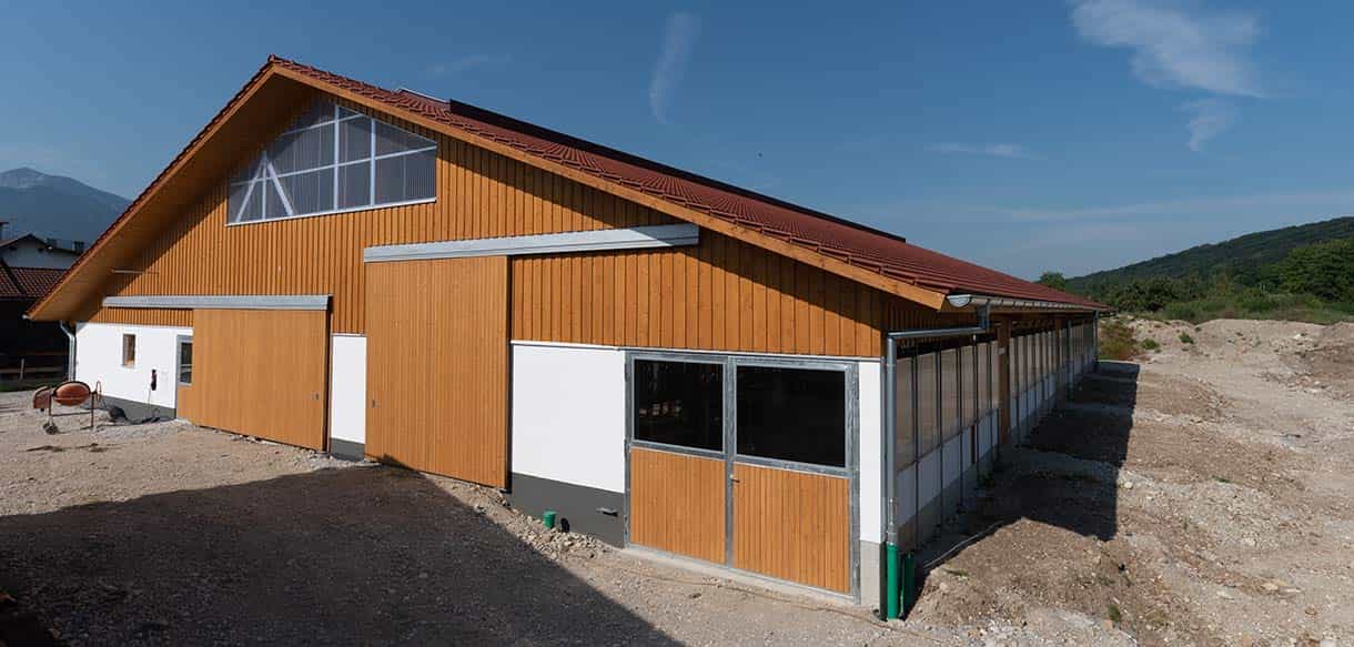 Milchviehstall in Großweil mit Holzfassade und Lichtband im Giebel vor Bergkulisse