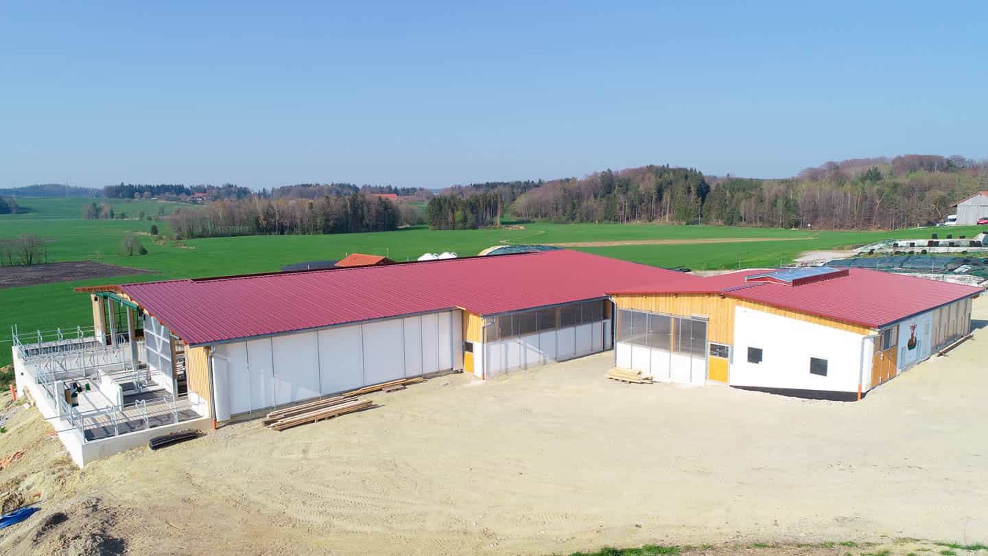 Gesamtansicht des Jungviehstalls in Rechtmehring mit rotem Dach in grüner Hügellandschaft