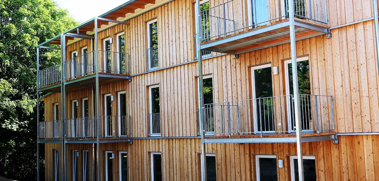 Balkone mit Stahlgeländern an der Holzfassade des dreigeschossigen Sozialwohnungsbaus von Haas Fertigbau