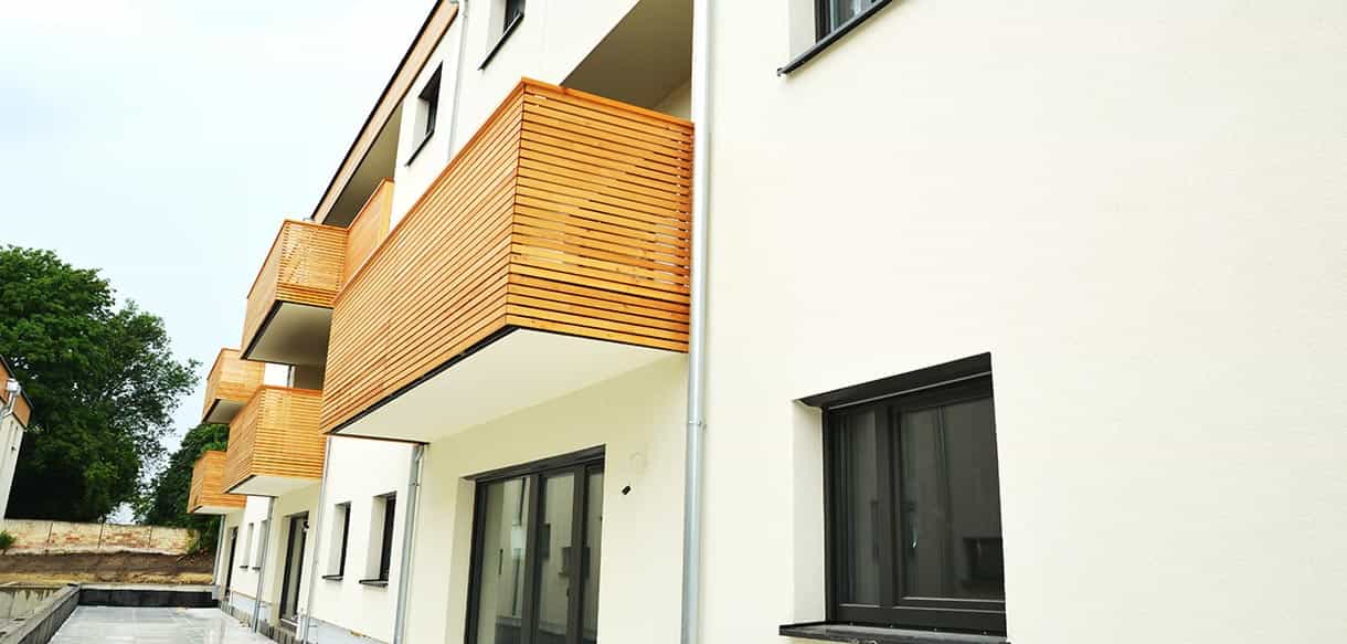 Außenansicht der Wohnhausanlage Mistelbach mit auskragendem Holzbalkon und weißer Putzfassade