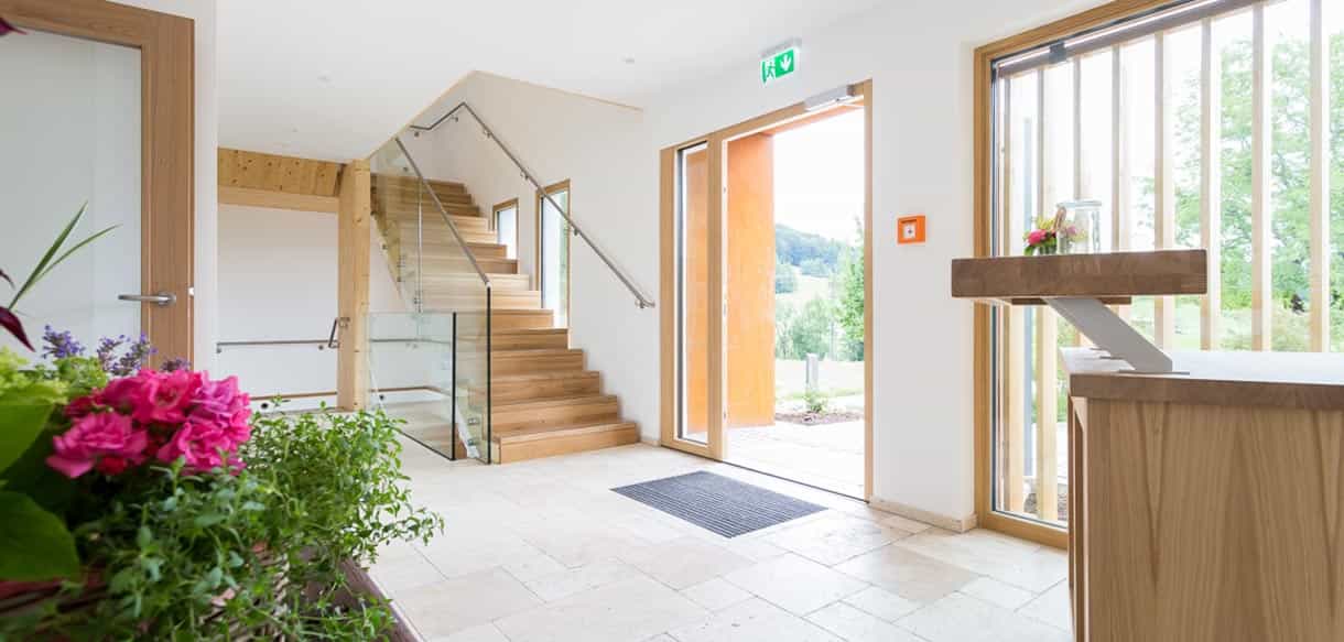 Eingangsbereich mit heller Holztreppe und Glasgeländer in der Pension Moarhof von Haas Fertigbau
