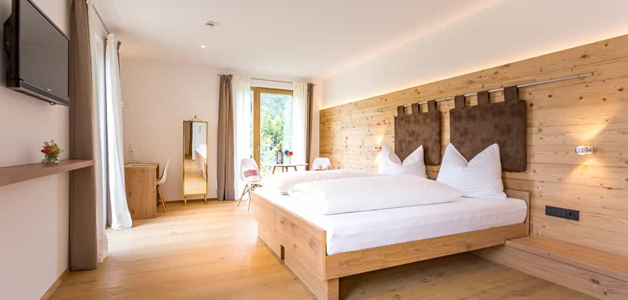 Helles Zimmer mit Holzwand hinter dem Doppelbett und Fenster zum Garten in der Pension Moarhof