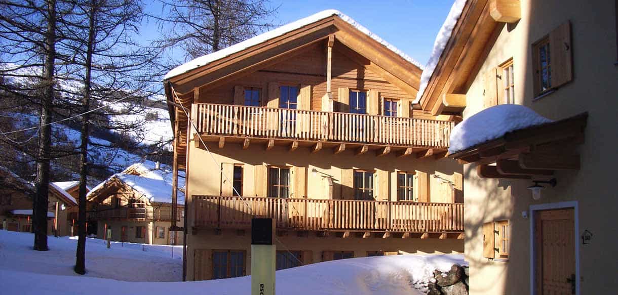Chalet mit Holzbalkonen und verschneitem Dach in der Ferienwohnanlage Pragelato von Haas Fertigbau