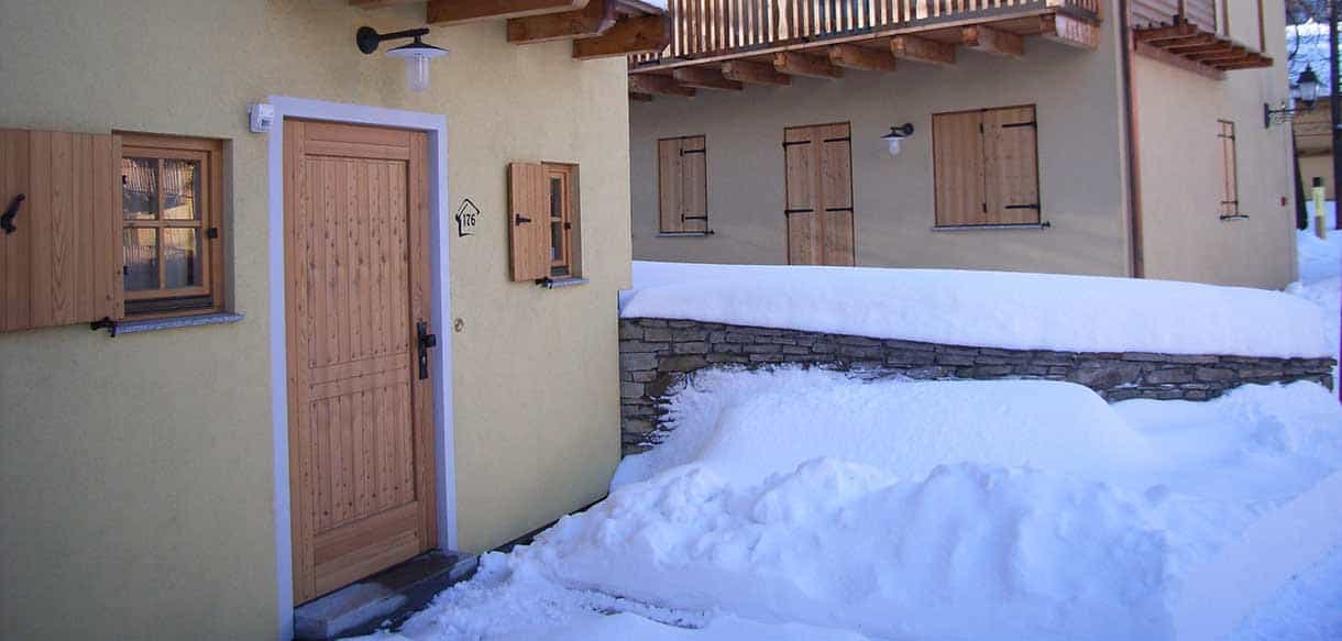 Holzeingangstür mit Natursteinsockel im Schnee an einem Chalet der Ferienwohnanlage Pragelato